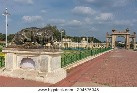 Mysore India - October 27 2013: Combination of brown East gate and dark brown bronze statue of aggressive lioness in front garden of Mysore Palace under cloudscape.