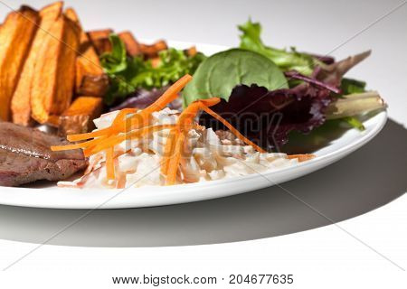 Home made cloeslaw with a steak dinner. Grated carrot on cole slaw. Classic steak and chips pub meal with homemade coleslaw in close up.