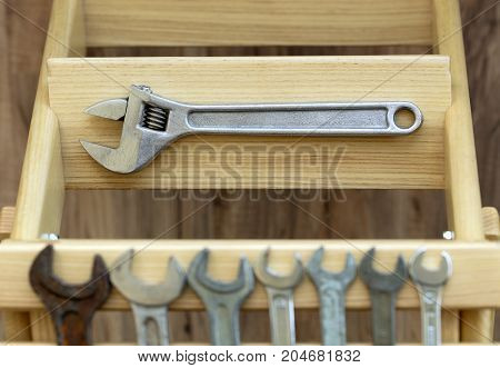Old adjustable wrench lies on the step of a wooden ladder against the background of old wrenches