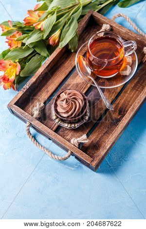 Picture of light breakfast, black tea, cupkake with cream and orange flowers on wooden tray