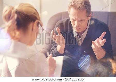 Being in despair. Depressed cheerless pleasant man sitting opposite his psychologist and complaining about his problems while suffering from depression