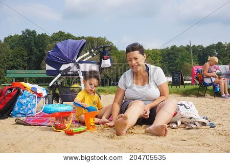 Woman And Toddler Boy Sitting On A Blanket And Playing With Toys At The Rosalka Lake Beach On August