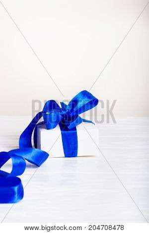 Christmas present gifts box on white wooden background. Gift birthday Christmas present concept - white gift box with blue ribbon on white painted wooden background