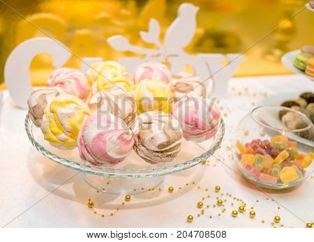 Colorful zephyrs on glass stand. Wedding or birthday candy bar. Pink yellow and brown marshmallow. Homemade sweet zephyr