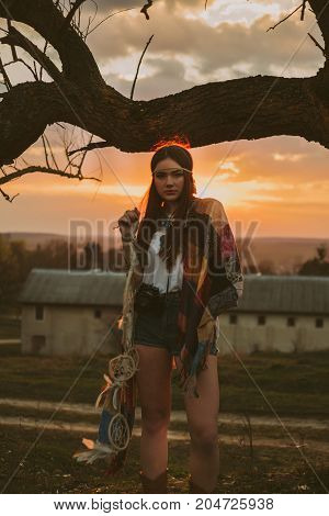 hipster girl standing near an old tree. the girl is holding the dreamcatcher.