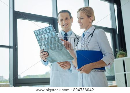 Pay attention here. Positive delighted intelligent woman standing together with her colleague and pointing at the X ray scan while discussing a diagnosis with him