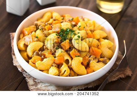Macaroni pasta with creamy pumpkin and mincemeat sauce garnished with parsley served in white bowl photographed with natural light (Selective Focus Focus in the middle of the dish)