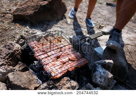 A young couple is traveling in the mountains. Summer journey of lovers, a guy frying meat at a bonfire for a girl. Healthy way of life, travel, summer vacation. The best pastime in the summer.