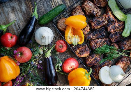 High Angle View of Grilled Meal of Steak, Chicken and Vegetables Spread Out on Rustic Wooden Table at Barbeque Party. Grilled meat and vegetables on rustic wooden table. Summer picnic time.