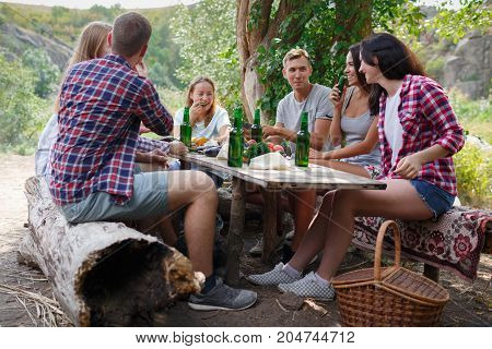 Friends interacting while having picnic in park on a sunny day. Leisure, holidays, eating, people and food concept - happy friends having dinner at the summer party. Best time for a picnic.