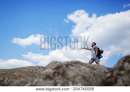 The guy looks into the distance, standing on the mountain. Beautiful mountain view on the background. Man in search of a way. Summer trip through the mountains without a map. Summer time.