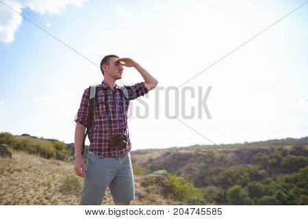 The guy looks into the distance, standing on the mountain. Beautiful mountain view on the background. Man in search of a way. Summer trip through the mountains without a map. Summer time.