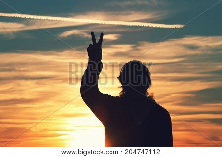 a woman giving a peace sign at sunset.