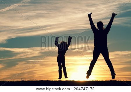 a mother with her child jumping at sunset.