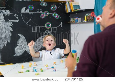 Cute little playfull toddler boy amazed by milky bubbles at child therapy session. Private one on one homeschooling with didactic aids.