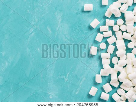 Marshmallows on blue background with copyspace. Flat lay or top view. Background or texture of colorful mini marshmallows. Winter food background concept.