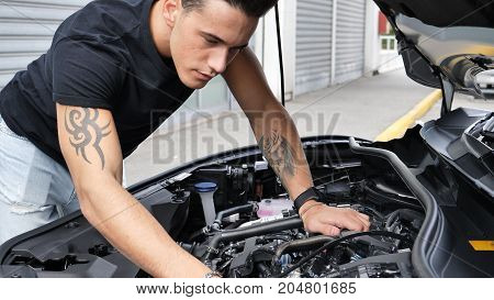 Handsome young man trying to repair a car engine, looking inside open bonnet
