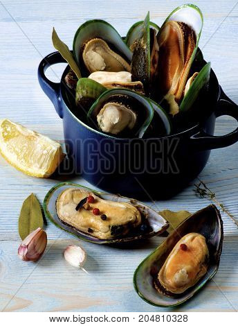 Arrangement of Fresh Boiled Green Mussels with Spices and Lemon in Dark Pannikin closeup on Blue Wooden background