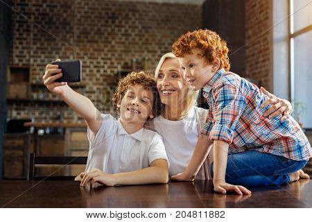 Memorable moment. Side view on a happy family members meeting at a dinner table and grinning broadly while taking a self portrait picture on a smartphone.