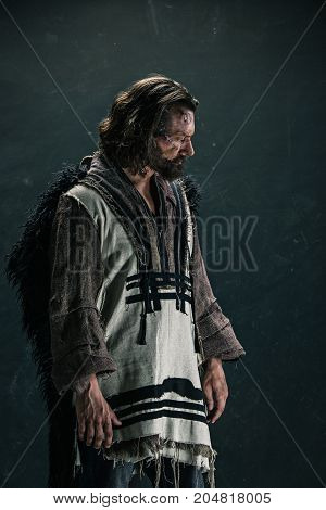 Actor in makeup, a poor man on black studio background. The bum in canvas rags. concept of vagrancy and survival