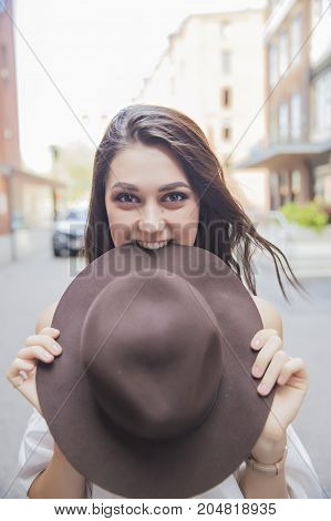 laughing girl hiding behind a hat. I'll eat my hat. cute young woman smiling and biting hat. the concept of a promise to eat a hat. Vertical