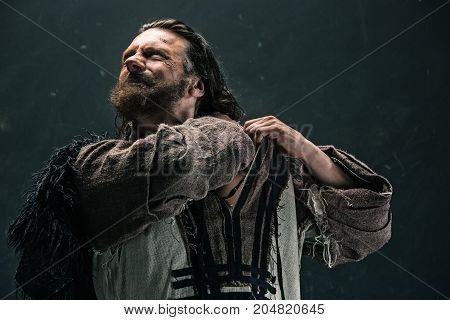 Actor in makeup, a poor man on black studio background. The bum in canvas rags. concept of vagrancy and survival. concept of pain and suffering