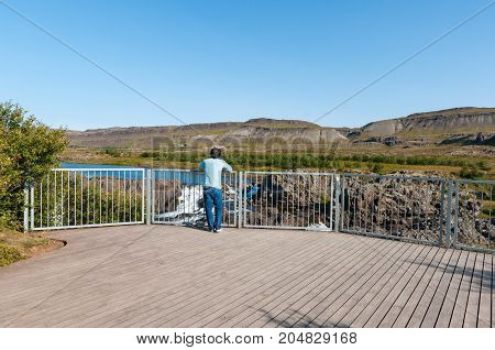 tourist enjoying the view from sightseeing platform near Waterfall Glanni in Nordura River in Borgarfjordur in Iceland