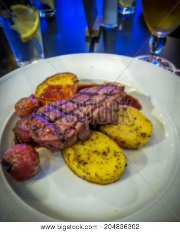 Blured view of appetizing grilled beef steak and onion with baked potato served on white plate. Menu photo.
