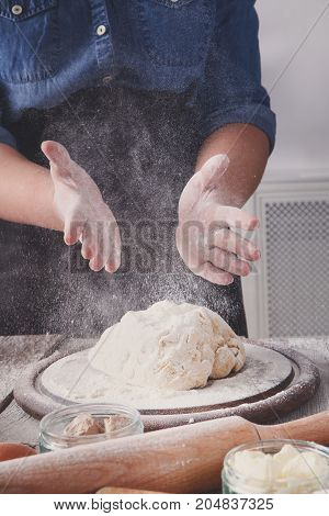 Baking concept, sprinkle flour on yeast dough. Flour, milk, and eggs on wooden cutting board, pastry ingredients. Cropped image of unrecognizable woman knead. Female baker closeup, vertical