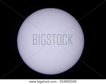 the sun viewed through a solar filter in a telescope with sunspot visible