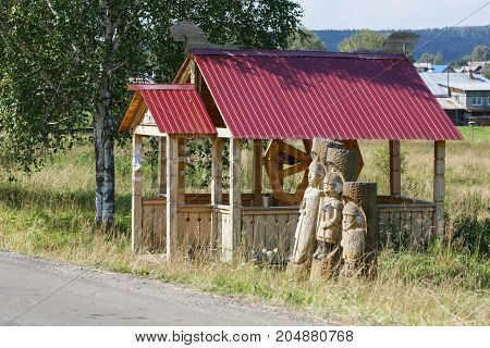 VISIM/ RUSSIA - JUNE 22, 2015. Wooden well and statues of the three Russian heroes in the old believer village Visim. Sverdlovsk region, Russia.