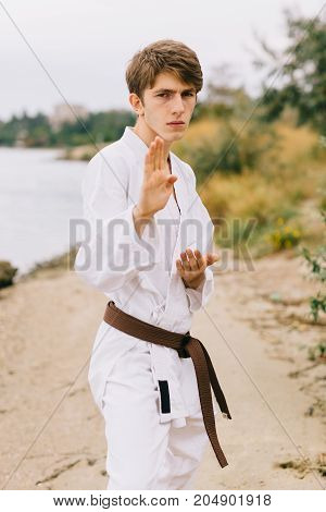 Young professional karate fighter in a blocking position. Boy on a jui-jitsu training on a blurred natural background.