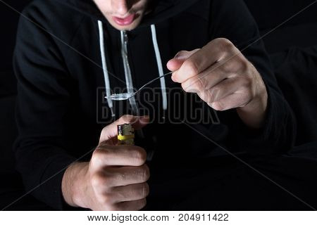 The young drug addict prepares heroin with spoon and lighter