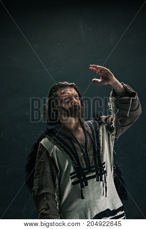 Actor in makeup, a poor man on black studio background. The bum in canvas rags. concept of vagrancy and survival