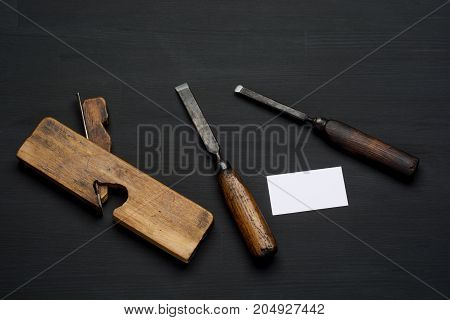 Woodworking tool on dark wooden background. chisel, plane and empty business card