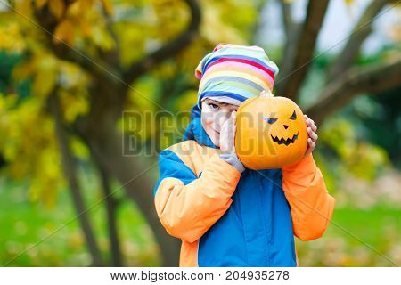 Happy cute little kid boy with halloween pumpkin lantern. Funny child in colorful clothes having fun and playing in autumn garden on cold autumnal day. Scary jack-o-lantern, celebration of holiday
