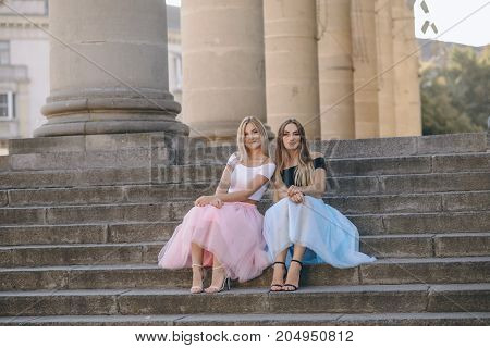 Two beautiful girls in colored skirts sit on stairs