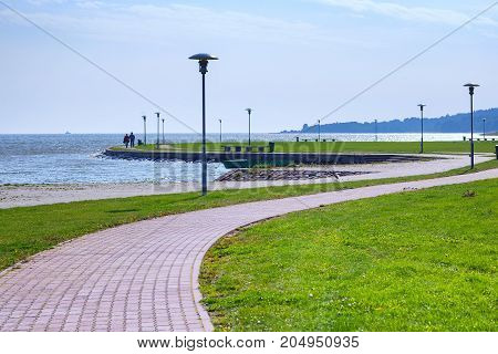 A sailing yacht runs along the shore with a green lawn and slender lanterns. Neringa