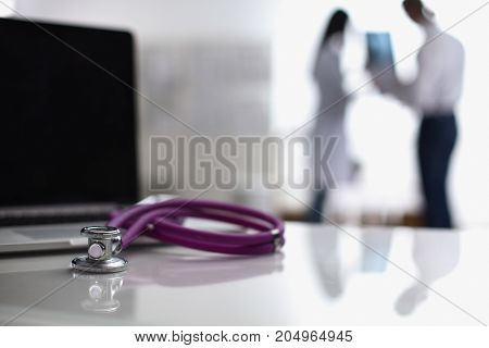 Laptop and medical stethoscope on the desk , doctors standing in the background.