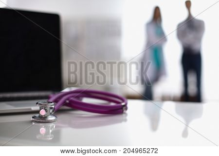 Laptop and medical stethoscope on the desk , doctors standing in the background.