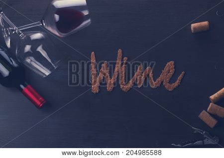 Bottle of red wine and two wine glasses on table with wine word letters, retro toned