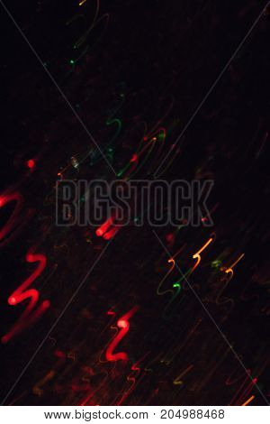 Abstract background of colorful crankles in motion on black. Bokeh of defocused curves, blurred neon yellow, green and red leds, festive backdrop of fireworks, holidays and celebrations