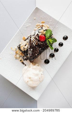 Chocolate pie on white square cut plate with decoration from cherry, almond and mint. Delicious dessert serving in restaurant with ice-cream ball, top view close up