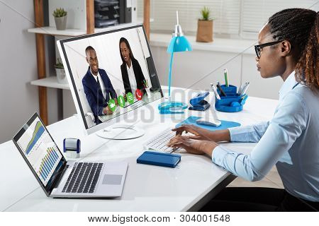 African Businesswoman Analyzing Graphs While Videoconferencing With Her Colleagues In Office