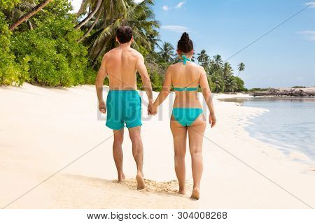 Rear View Of A Young Couple Together Walking On Beach