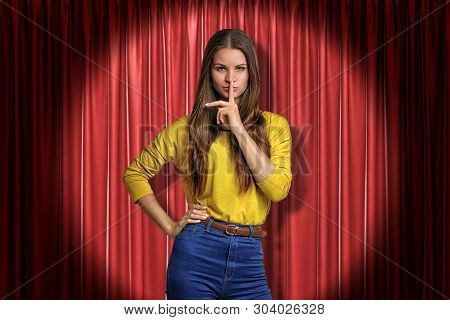 Front Crop View Of Pretty Woman Standing In Spotlight At Red Stage Curtain, One Hand On Hip, Other H