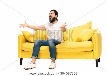 Bearded Latin Man Watching Championship While Sitting On Sofa And Gesturing Isolated On White