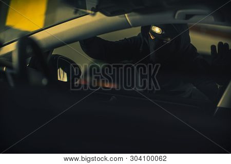 Car Thief Wearing Black Mask And Hood Looking For The Right Car To Steal. Vehicle Theft Illegal Acti