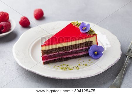 Raspberry Layerd Cake Decorated With Violet Flowers On White Plate. Grey Stone Background