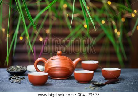 Green Tea In Tea Pot And Chawan Bowls, Cups. Outdoor Background With Bamboo Leaves And Bokeh Lights.